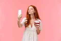 有吸引力的红色头发的人高加索人女庆祝生日发送升值追随者社会媒体采取自拍智能手机关闭眼睛褶皱嘴唇空气吻持有生日蛋糕