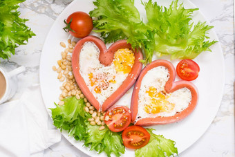 浪漫的早餐炸鸡蛋心形状的香肠生菜樱桃西红柿板表格前视图特写镜头