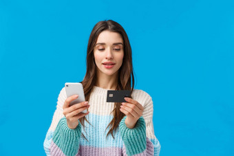 半身照肖像时尚的现代女人冬天毛衣使订单在线购物互联网插入信贷卡计费信息智能手机持有信贷卡移动蓝色的背景