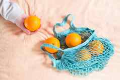 女手拉新鲜的橙子网袋织物背景浪费