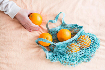 女人的手折叠新鲜的橙子网袋织物背景浪费
