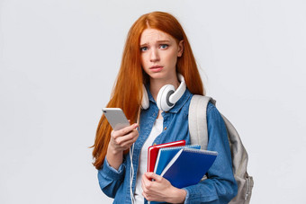 不<strong>安心</strong>烦意乱悲观的可爱的红色头发的人十几岁的女孩学生大学皱着眉头陷入困境的不开心相机持有背包教育笔记本电脑智能手机