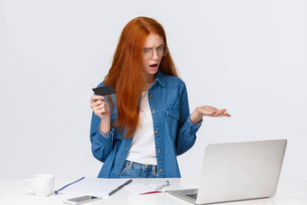 困惑困惑红色头发的人女人使在线购买不要问题转移钱occused耸指出沮丧移动PC屏幕持有信贷卡抱怨