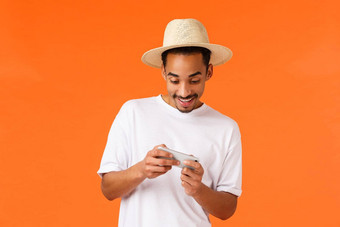 无忧无虑的快乐快乐的非裔美国人的男朋友玩智能手机游戏赛车说谎池假期移动车移动赢得水平微笑快乐橙色背景