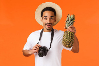 有魅力的年轻的有吸引力的非裔美国人旅游旅行者采取图片假期相机持有菠萝微笑快乐有趣的夏天奢侈品度假胜地橙色背景