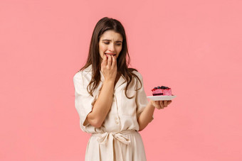 <strong>抵制</strong>诱惑年轻的女人饮食吃健康的食物咬美味的蓝莓蛋糕咬指甲盯着板站粉红色的背景欲望