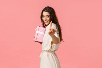 浪漫的关系假期概念可爱的诱人的女朋友准备特殊的礼物显示手指等待隐藏礼物盒子微笑惊喜现在粉红色的背景
