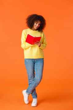 全身的垂直拍摄梦幻可爱的非裔美国人女学生非洲式发型发型休闲衣服大学使笔记站橙色背景写作笔记本微笑