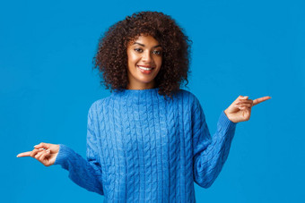 好愉快的华丽的非裔美国人女孩冬天毛衣建议变体指出手指横盘整理左广告片微笑快乐的蓝色的背景