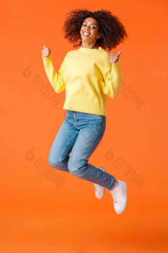 全身的垂直拍摄快乐满意无忧无虑的快乐的非裔美国人女人非洲式发型卷曲的发型跳快乐幸福显示竖起大拇指橙色背景