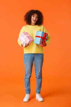 全身的垂直拍摄兴奋可爱的快乐非裔美国人女收到了礼物假期站逗乐很高兴持有包装礼物橙色背景