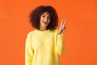 无忧无虑的可爱的愚蠢的非裔美国人女孩摆姿势照片橙色背景微笑显示和平标志奶酪感觉快乐的乐观的表达积极的情绪