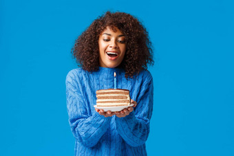 快乐梦幻充满希望的生日女孩使有吸引力的非洲美国女人卷曲的发型吸入空气吹出基斯蜡烛美味的生日蛋糕站蓝色的背景