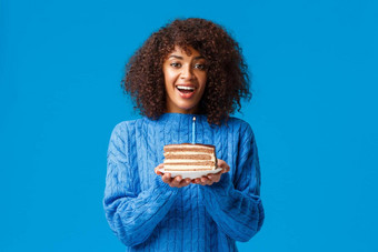 使真正的快乐的梦幻可爱的非裔美国人生日女孩持有蛋糕蜡烛<strong>熄灭</strong>微笑生日聚会，派对站毛衣蓝色的背景