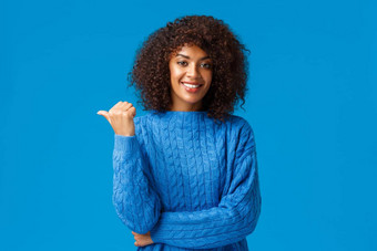 快乐友好的即将离任的漂亮的非裔美国人女冬天毛衣<strong>分享链接</strong>给建议指出拇指左退房广告微笑站蓝色的背景