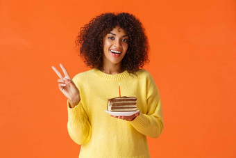 半身照肖像快乐非裔美国人女人黄色的毛衣显示和平标志奶酪生日女孩采取照片生日蛋糕蜡烛使站橙色背景