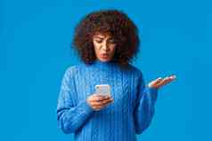 问题消息传递人概念困惑不高兴拉紧非裔美国人年轻的女人收到奇怪的消息盯着智能手机屏幕笨耸蓝色的背景