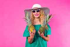 快乐年轻的女人持有菠萝粉红色的背景夏天饮食假期概念