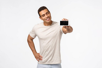 深刻的印象满意好看的拉美裔的家伙好形状促进健身应用程序移动屏幕很高兴微笑拉伸手持有智能手机做广告应用程序白色背景