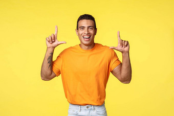 快乐快乐的年轻的高加索人的家伙橙色t恤微笑很高兴指出笑促进广告给建议推荐下载应用程序商店商店黄色的背景