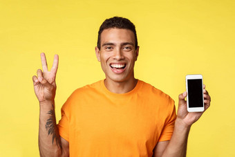 快乐的英俊的现代的家伙纹身手臂持有智能手机显示移动屏幕使和平标志微笑很高兴吹牛假期旅行照片建议应用程序促进在线商店