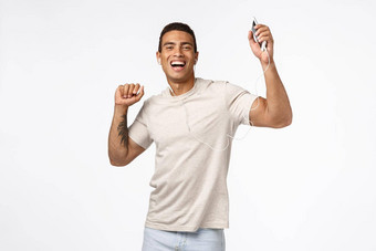 快乐的好看的巴西男人。纹身提高手跳舞无忧无虑的享受太棒了耳机位持有智能手机穿《<strong>连线</strong>》杂志耳机微笑快乐白色背景
