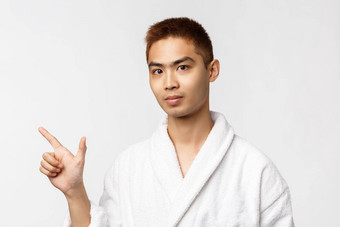 美水疗中心休闲概念肖像年轻的亚洲男人。<strong>邀请朋友</strong>热弹簧指出手指左相机显示广告穿浴袍白色背景