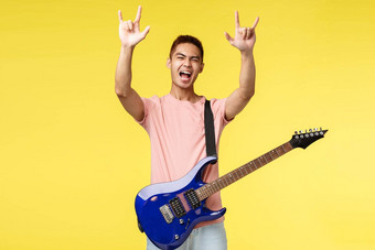 生活方式休闲青年概念好看的亚洲的家伙有趣的执行阶段持有电吉他显示<strong>摇滚手势</strong>大喊大叫热情的有趣的黄色的背景
