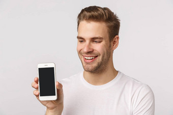 快乐的可爱的英俊的金发碧眼的有胡子的的男朋友白色t恤持有智能<strong>手机</strong>显示移动显示微笑很高兴吹牛个人社会媒体<strong>页面</strong>应用程序分数