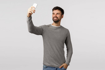 无忧无虑的好看的有胡子的高加索人的家伙采取自拍智能手机微笑很高兴会说话的视频在线信息的持有手口袋里拍摄过滤器应用程序白色背景