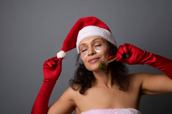 有吸引力的女人圣诞老人服装玉辊按摩器整容淋巴排水面部按摩皮肤护理美容概念圣诞节广告美客厅水疗中心