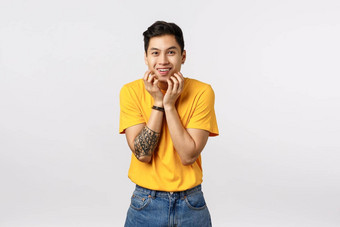 逗乐快乐的好看的亚洲年轻的男人。纹身穿黄色的t恤触碰下颌的轮廓咯咯地笑微笑深刻的印象传播流言蜚语听到令人印象深刻的谣言捕捉新鲜的新闻
