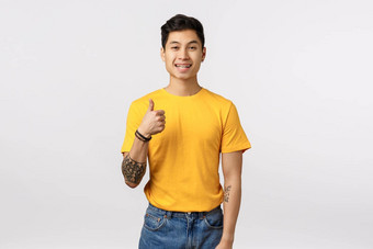 好的想法让热情的英俊的亚洲纹身的家伙黄色的t恤显示竖起<strong>大拇指</strong>批准手势微笑点头协议同意白色背景