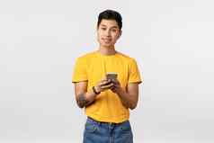 英俊的时尚的亚洲男人。黄色的t恤牛仔裤穿无线耳机持有智能手机听音乐使播放列表应用程序唱歌卡拉ok电话应用程序白色背景