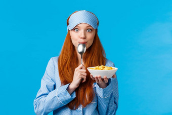 嗯美味的可爱的漂亮的狡猾的少年大学女孩舔勺子吃美味的谷物持有板早餐穿睡眠面具睡衣早....站蓝色的背景