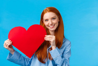 温柔护理浪漫概念浪漫的好看的红色头发的人女睡衣给感情爱持有红色的心标志微笑站蓝色的背景