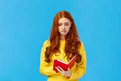 困惑不安有关可爱的红色头发的人女学生麻烦时间表皱着眉头阅读女朋友日记感觉有罪持有红色的笔记本感觉陷入困境的蓝色的背景