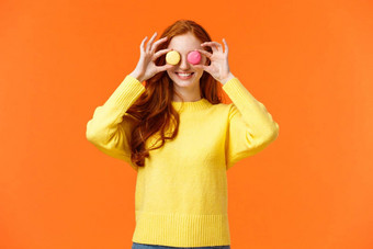 时尚食物消费者概念快乐的愚蠢的红色头发的人女人愚弄玩甜点使眼睛马卡龙微笑快乐站橙色背景