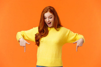 想知道兴奋逗乐可爱的红色头发的人女人黄色的毛衣指出手指底微笑退房产品促销冬天假期事件橙色背景