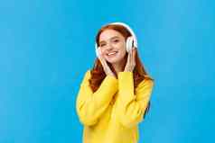 时尚有吸引力的无忧无虑的红色头发的人女人黄色的毛衣听音乐耳机微笑倾斜头快乐收到耳机圣诞节礼物站蓝色的背景