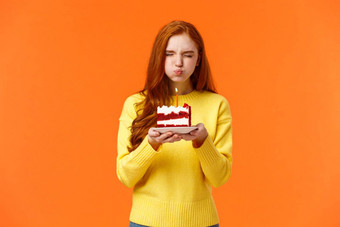 可爱的愚蠢的可爱的红色头发的人生日女孩关闭眼睛持有生日一块蛋糕撅嘴打击蜡烛使梦想真正的关闭眼睛庆祝朋友橙色背景