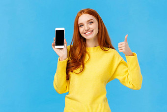 女孩显示好应用程序推荐下载应用程序可爱的红色头发的人女人黄色的毛衣冬天假期出售在线商店显示智能手机显示蓝色的背景