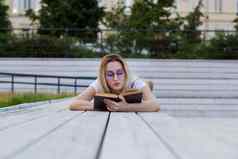 年轻的女人赶时髦的人阅读书说谎板凳上夏天