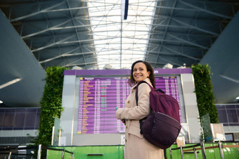 美丽的中间东部女人旅行者背包微笑露出牙齿的微笑肩膀站前面飞行时间表信息面板国际机场