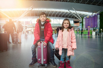 快乐美丽的欧洲孩子们温暖的衣服英俊的男孩坐在手提箱年轻的妹妹可爱的女孩国际机场家庭飞机旅行概念