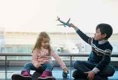 可爱的孩子们男孩女孩玩玩具飞机坐着地板上全景窗户俯瞰跑道飞机离开终端国际机场