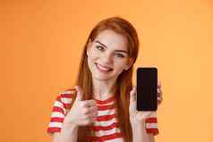 智能手机应用程序保证自信的可爱的友善的红色头发的人女人推荐手机应用程序介绍在线商店网站给翘拇指批准站橙色背景
