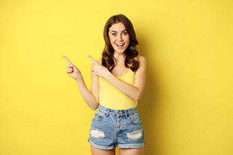 肖像时尚的夏天女孩浅黑肤色的女人女人显示指出手指左广告站黄色的背景