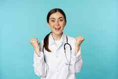 快乐兴奋年轻的女医生医生庆祝实现目标微笑很高兴赢得站白色外套蓝色的背景