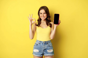 漂亮的浅黑肤色的女人女人显示移动电话屏幕智能手机应用程序接口标志推荐网站商店站黄色的背景